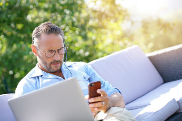 Cool businessman working with laptop and headset outside the office