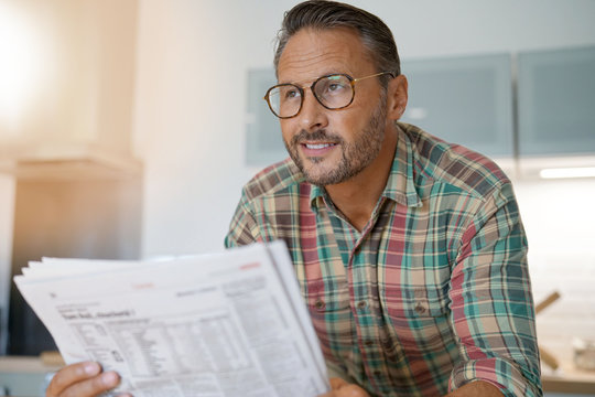 Handsome mature man at home reading newspaper