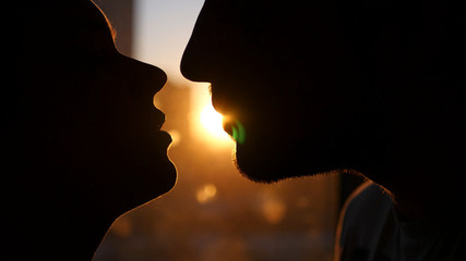 Young couple in love, look into each other's eyes, against the sunset, with the effect of a lens. He runs a finger down his face.