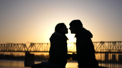 A loving couple, happy man and woman are kissing on the background of a railway bridge and sunset.
