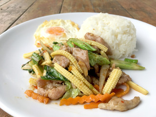 mixed vegetable stire-fried with meat and fried egg with rice in white dish on wooden background. Thai Food for health.