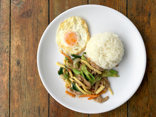 mixed vegetable stire-fried with meat and fried egg with rice in white dish on wooden background. Thai Food for health.