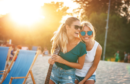 Two young female friends hangout at the  beach ,singing and relaxing in beautiful summer sunset.They hug each other.Best friends.