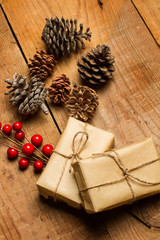 Obraz na płótnie Canvas Cajas de regalo de Navidad junto con piñas y acebo sobre fondo de madera rústico. Vista superior y de cerca. Formato vertical