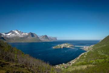 Scenic view of remote town of Husoy, Senja Norway with snowy peaks in distance.