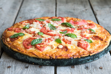 Hot Homemade Pepperoni Pizza on a rustic wooden table. Pizza with tomato, cheese and basil 