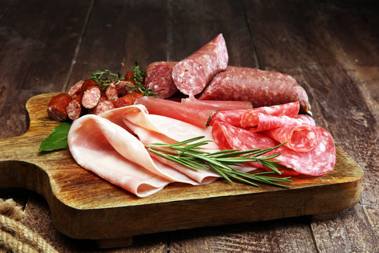 Marble cutting board with prosciutto, bacon, salami and sausages on wooden background. Meat platter