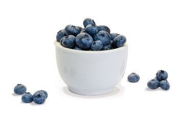 Closeup  blueberry in white ceramic cup  and small piles of blueberry on white background isolated