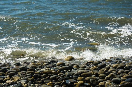 Fototapeta rocky sea shore with pebble beach, waves with foam