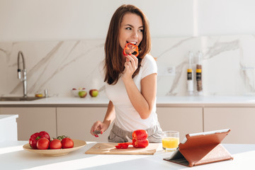 Young smiling woman eating vegetables while making a salad