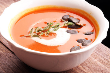 Roasted pumpkin and carrot soup with cream and pumpkin seeds on wooden background.