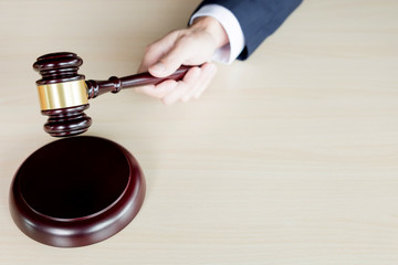hand of Judge's holding wooden hammer knocking a gavel against wooden background