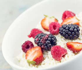Organic cottage cheese with blackberry, strawberry and raspberry in a white ceramic bowl on the kitchen table. Dairy products for the breakfast. Healthy food concept.
