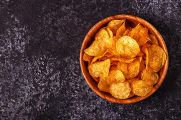 Crispy potato chips in a bowl on stone background.