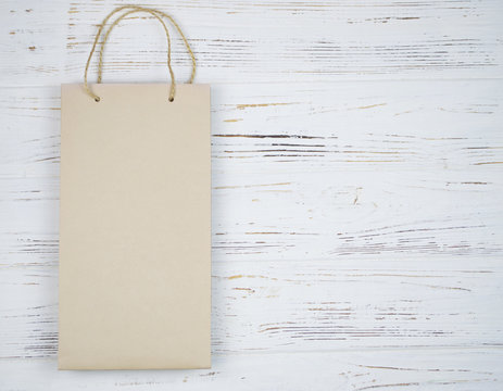 Beige paper bag with handles on white wooden background.
