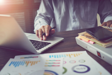 businessman hand working laptop on wooden desk in office in morning light. The concept of modern work with advanced technology. vintage effect