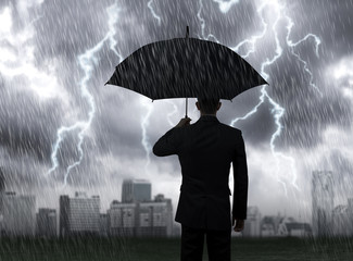 Businessman hold black umbrella standing under rain storm lightning with city background