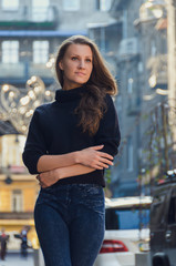 Stylish, slender, confident woman stands on the city street in black sweater,