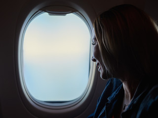 Fototapeta na wymiar Young beautiful woman looking into the airplane window