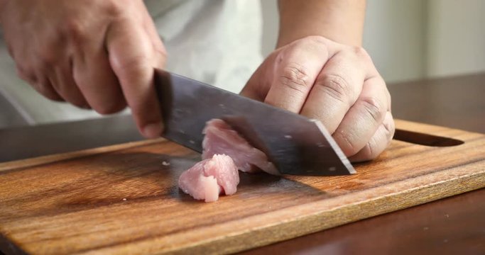 Close up the human hand cutting raw pork on wooden chop board in kitchen room , 4K Dci resolution