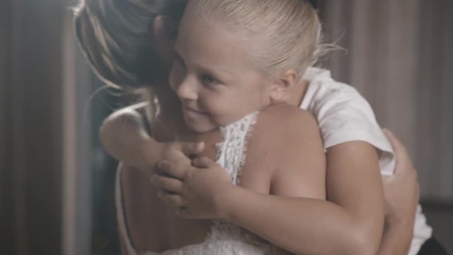 Little sweet girl hugs her mom tightly and closes eyes with pleasure. A girl is an actress or a dancer with her hair tucked away in the arms of her mother. The concept of parental pride and support.