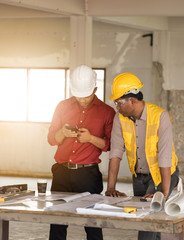 Team of architects engineer working together Asian businessman with blueprint and Craftsman tool on table at construction site.using smart phone consult something.