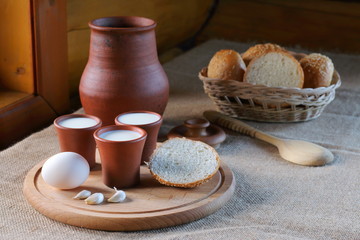 Cups with milk and a wicker basket with bread. Clay cups with milk and a wicker basket with bread are on the table near the window in the village house.