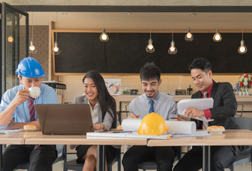 Team of architects engineer working together Asian businessman with blueprint and Craftsman tool on table at construction site.using smart phone consult something.