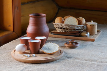 Cups with milk and a wicker basket with bread. Clay cups with milk and a wicker basket with bread are on the table near the window in the village house.