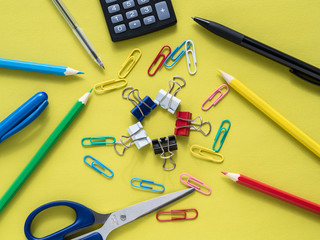 Colorful stationery on yelow background - calculator, scissors,  crayon, pencil, pen