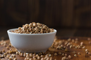 Buckwheat grain on ceramic bowl over wooden table.