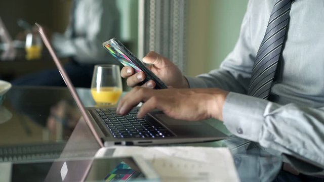 Businessman working with smartphone and laptop sitting by table at home
