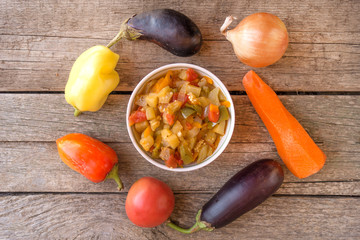 Stew in the bowl and aubergines, tomatoes, onions, carrots and peppers on the center of wooden...