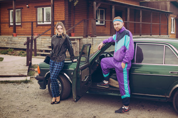 Guy and girl in clothes of the nineties, next to the old car