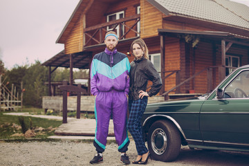 Guy and girl in clothes of the nineties, next to the old car - obrazy, fototapety, plakaty