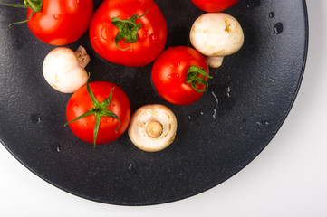 fresh tomatoes and mushrooms - champignons on black plate
