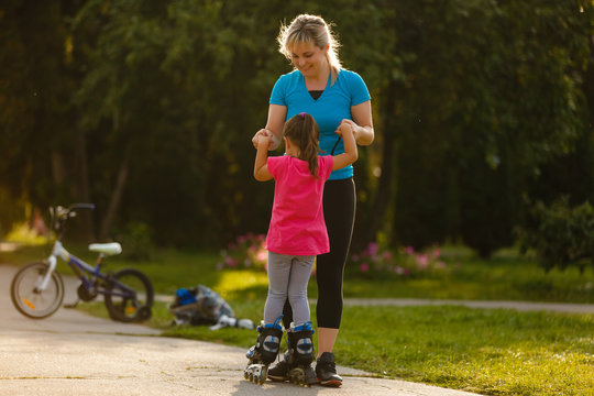 mother teaching daughter rollerblade skating in the park