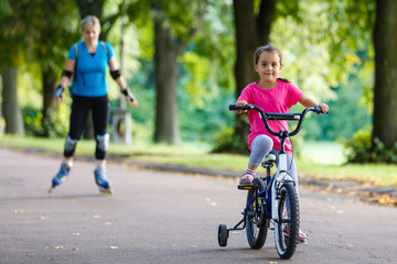 A young mother roller skating. her Daughter riding a bicycle