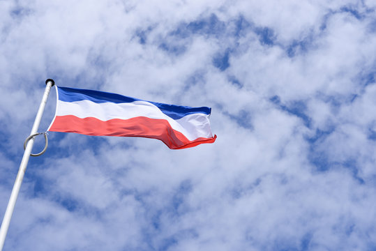Fahne oder Flagge der Niederlande vor einem bewölkten blauen weißen Himmel wehende