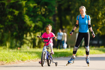 A young mother roller skating. her Daughter riding a bicycle