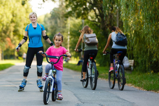 A young mother roller skating. her Daughter riding a bicycle