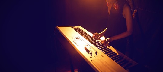 Female musician playing piano keyboard in illuminated club