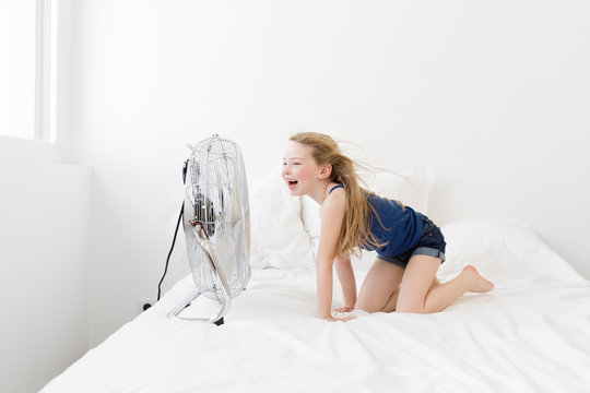 smiling girl on bed facing a fan