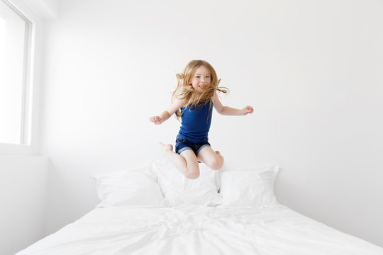 Smiling young girl jumping on white bed
