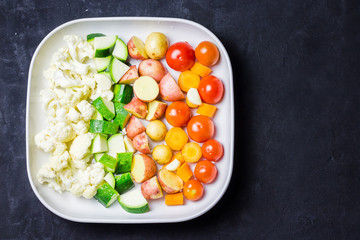 Raw vegetables in a baking dish on dark background. Top view, copy space.