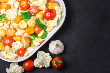 Raw vegetables - tomatoes, cauliflower, zucchini, potato with oil and herbs in white baking dish. Top view, space for text.