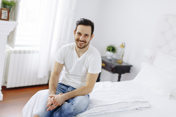 Smiling young man sitting on the bed in the bedroom