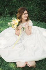 Lovely bride sitting on ground holding a bouquet smiling at camera