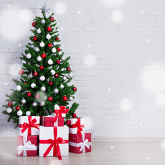 Fototapeta na wymiar Decorated christmas tree with colorful balls and gift boxes over white brick wall and snowfall