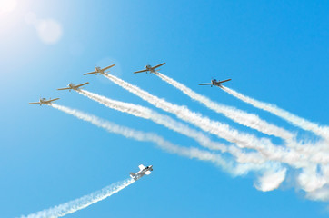 Light engine airplane with a trace of white smoke fly in groups in the blue sky with sunlight and glare